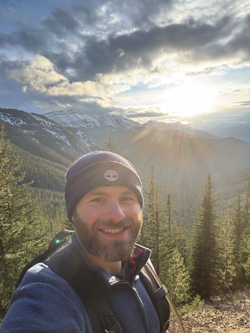 Cameron smiling on a forested mountain trail at sunset
