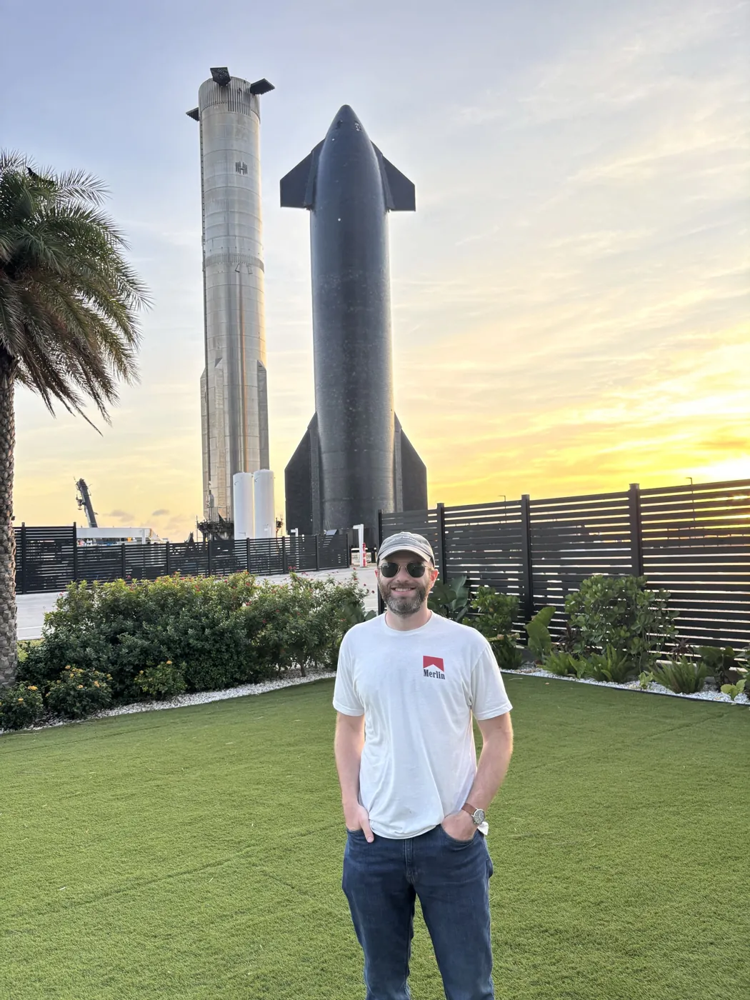 Cameron in a Merlin shirt standing in front of Starship and Super Heavy